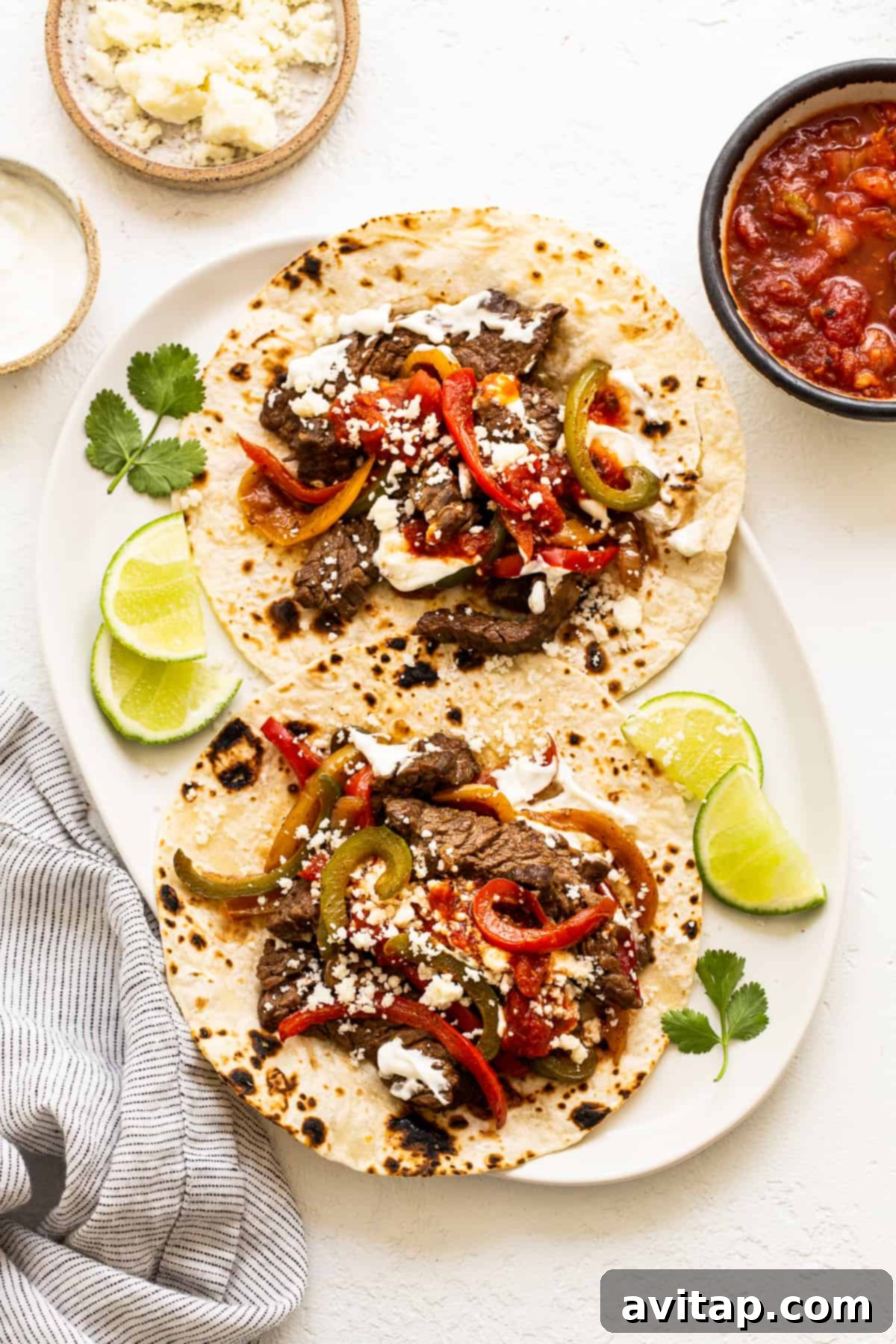 Finished steak fajitas on a plate, generously topped with cotija cheese and fresh cilantro.