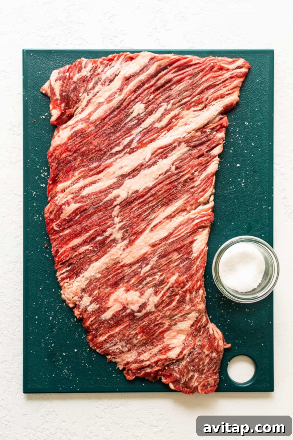 Raw flank steak on a wooden cutting board, perfectly prepared for slicing.