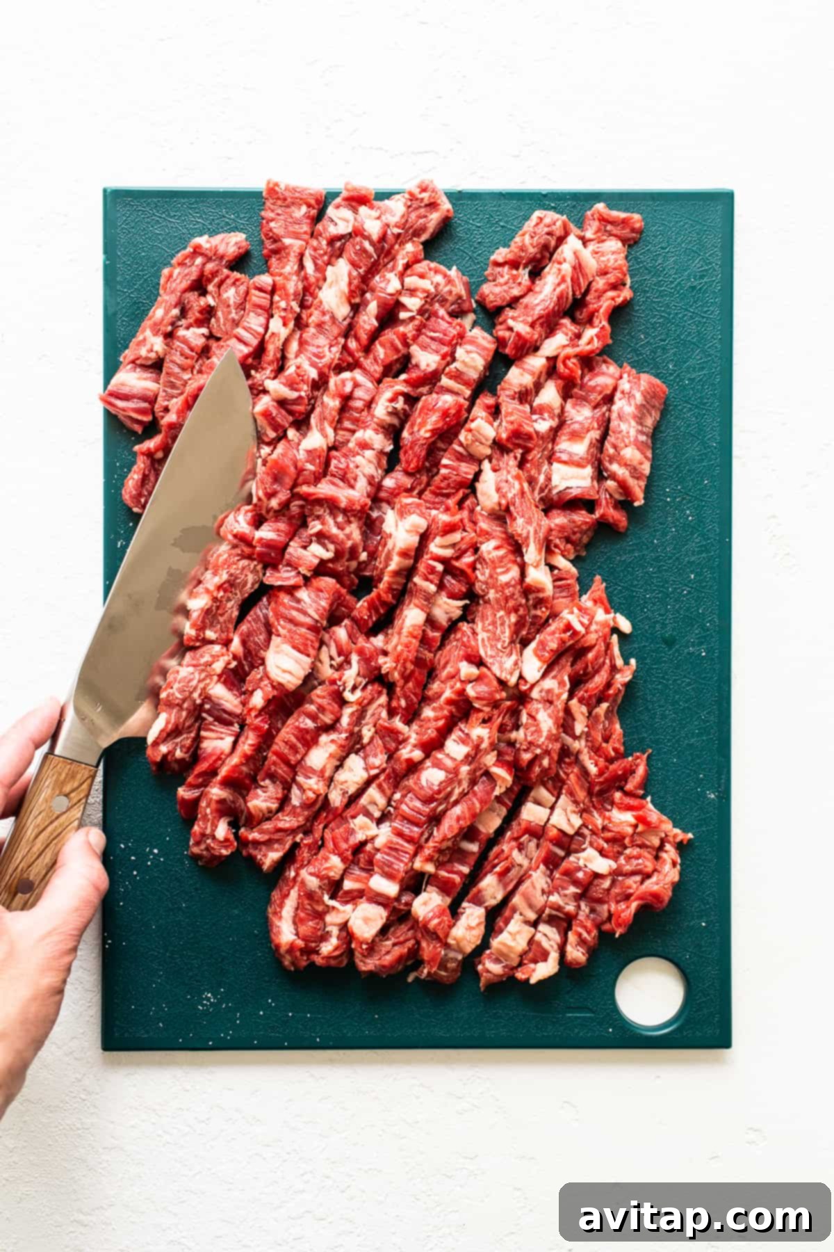 Thinly sliced flank steak on a cutting board, cut against the grain for maximum tenderness.