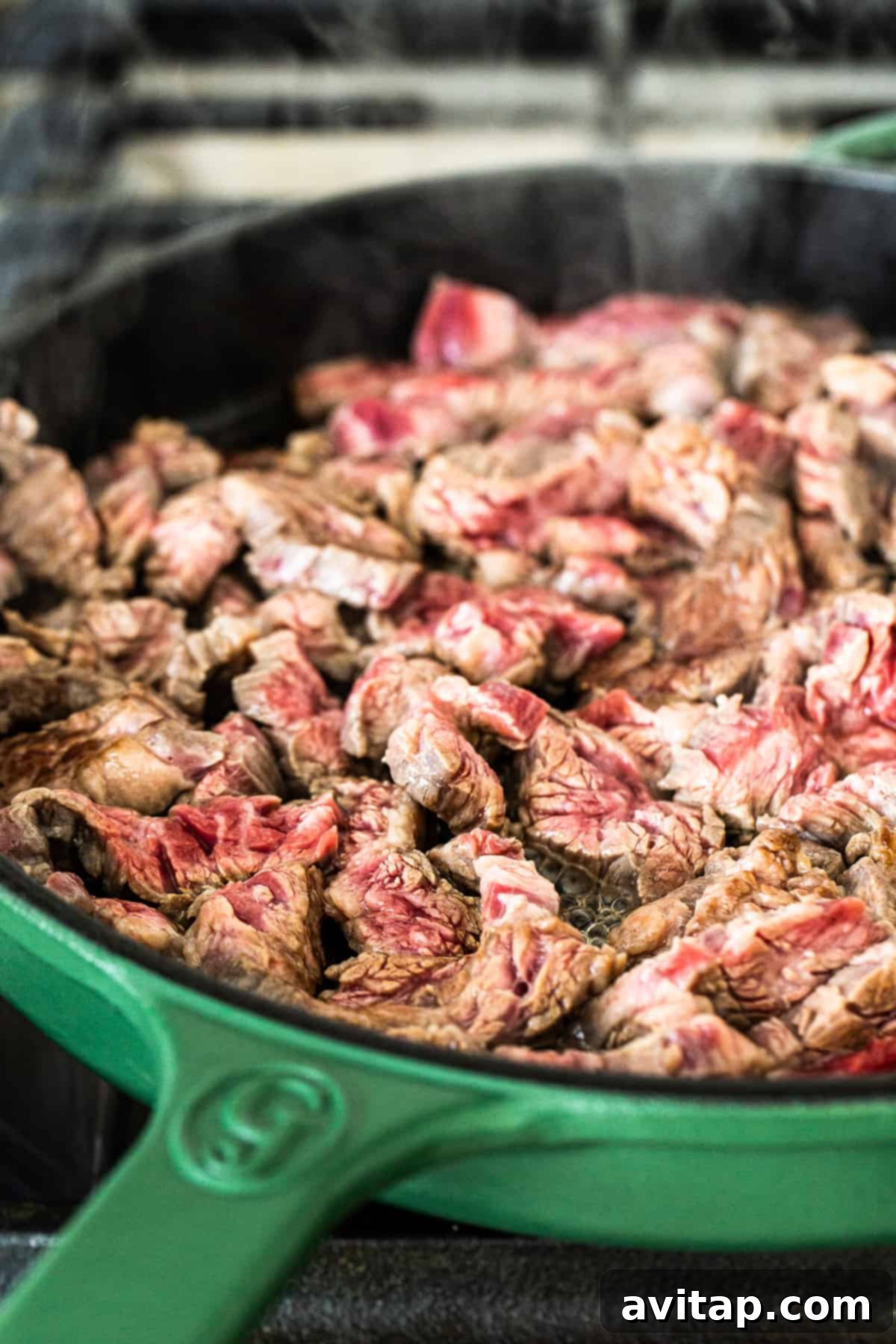 Sizzling flank steak strips cooking in a cast iron skillet, showing perfect browning and slight pink in the center.