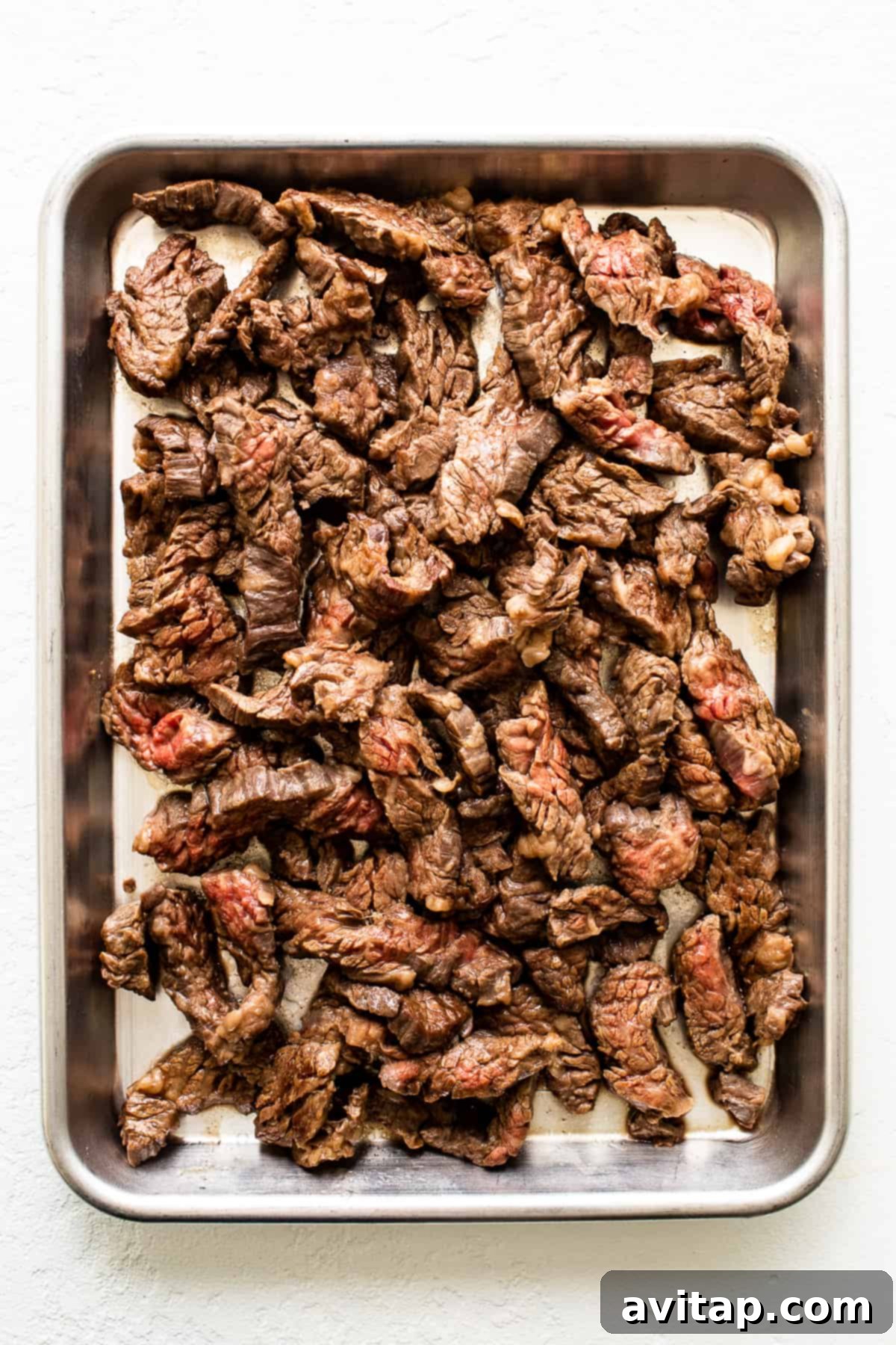 Cooked flank steak strips resting on a baking sheet, showcasing their tender texture and seasoning.