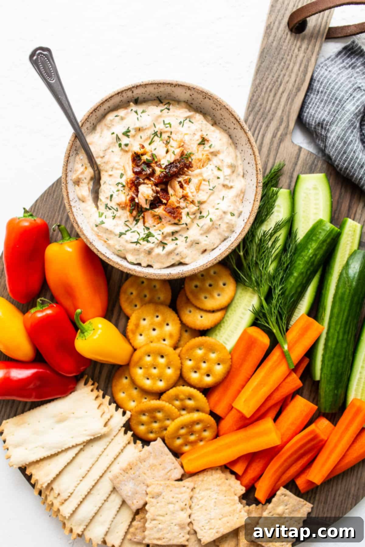 A vibrant platter featuring a bowl of smoked salmon dip surrounded by an assortment of crisp crackers and fresh, colorful vegetables.