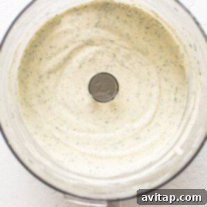 A food processor filled with a pale green, creamy sauce, showcasing the blended base ingredients.