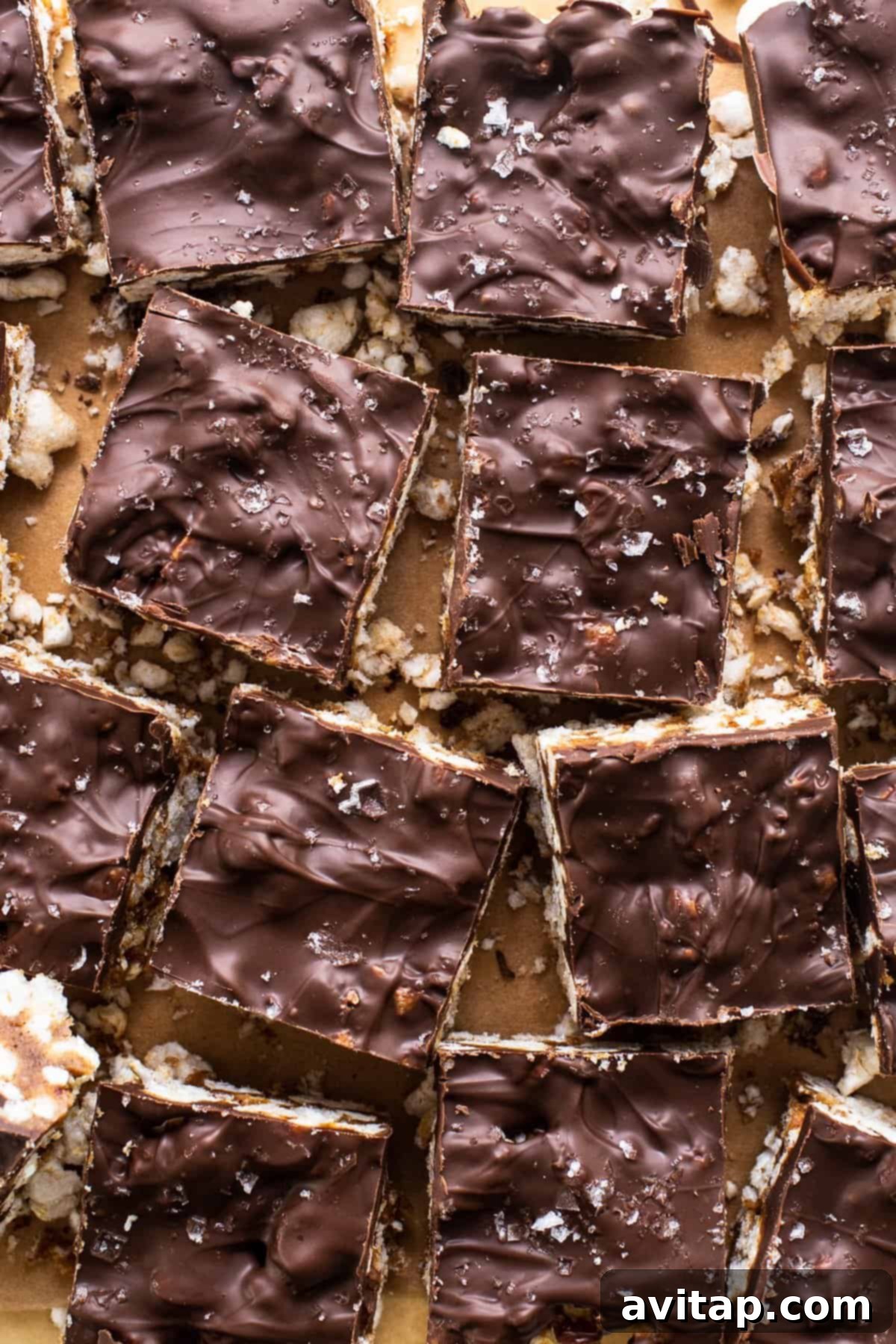 A tray of perfectly arranged chocolate covered rice cake magic bars on a rustic wooden table, garnished with a sprinkle of sea salt.