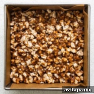 Caramel popcorn pressed into a pan on a white surface, illustrating the base layer being flattened.