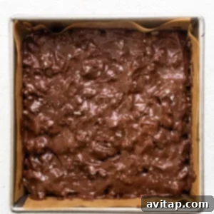 Chocolate fudge brownies in a baking pan, showing the chocolate topping being spread smoothly.