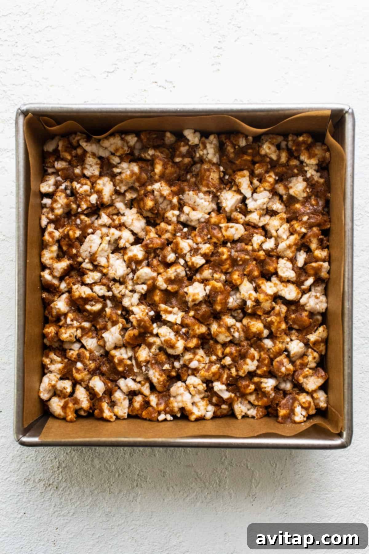 A saucepan on a pristine white surface, containing a glossy, melted mixture of almond butter and honey, ready to be combined with the rice cakes.