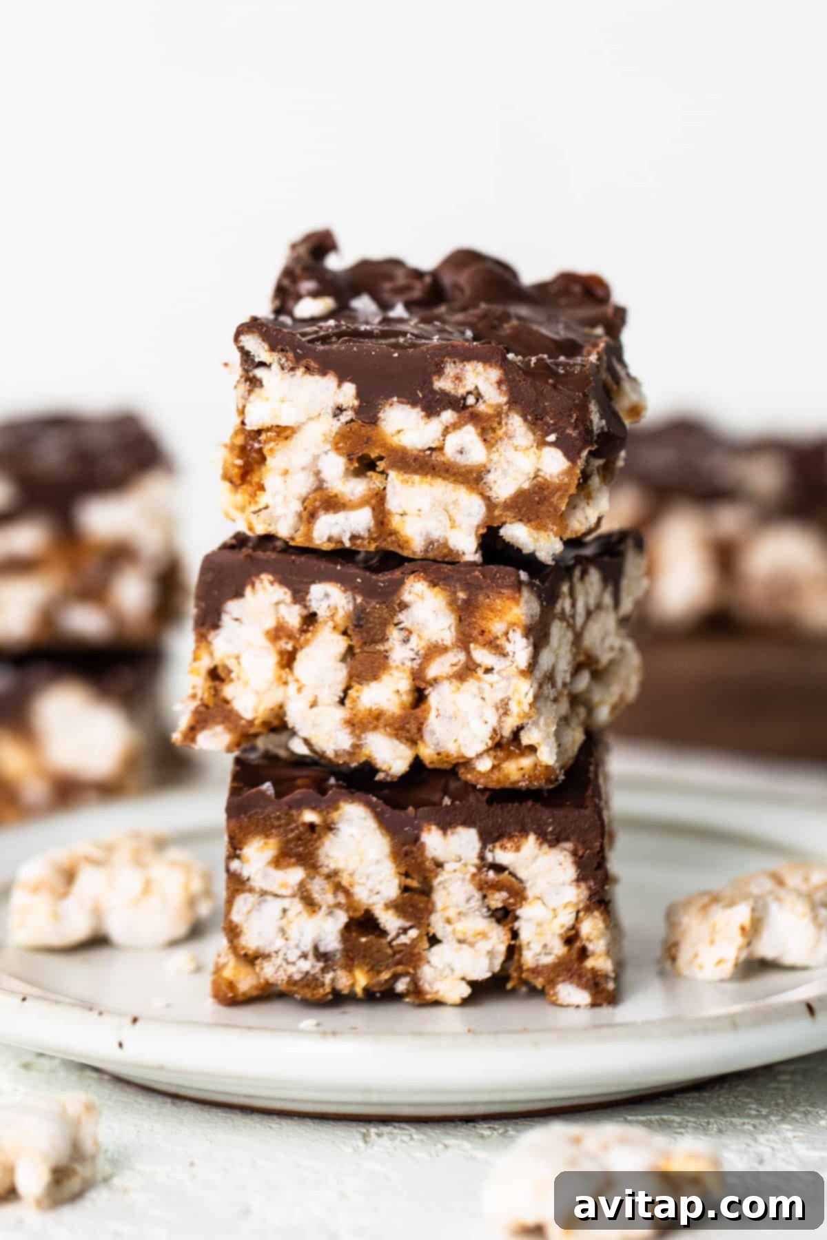 A stack of perfectly sliced chocolate-covered squares on a white plate, showcasing the crispy rice cake base and rich topping.