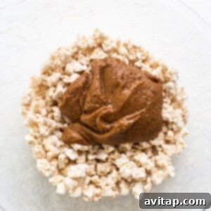 A bowl of granola with peanut butter coating, illustrating the mixture being combined thoroughly.