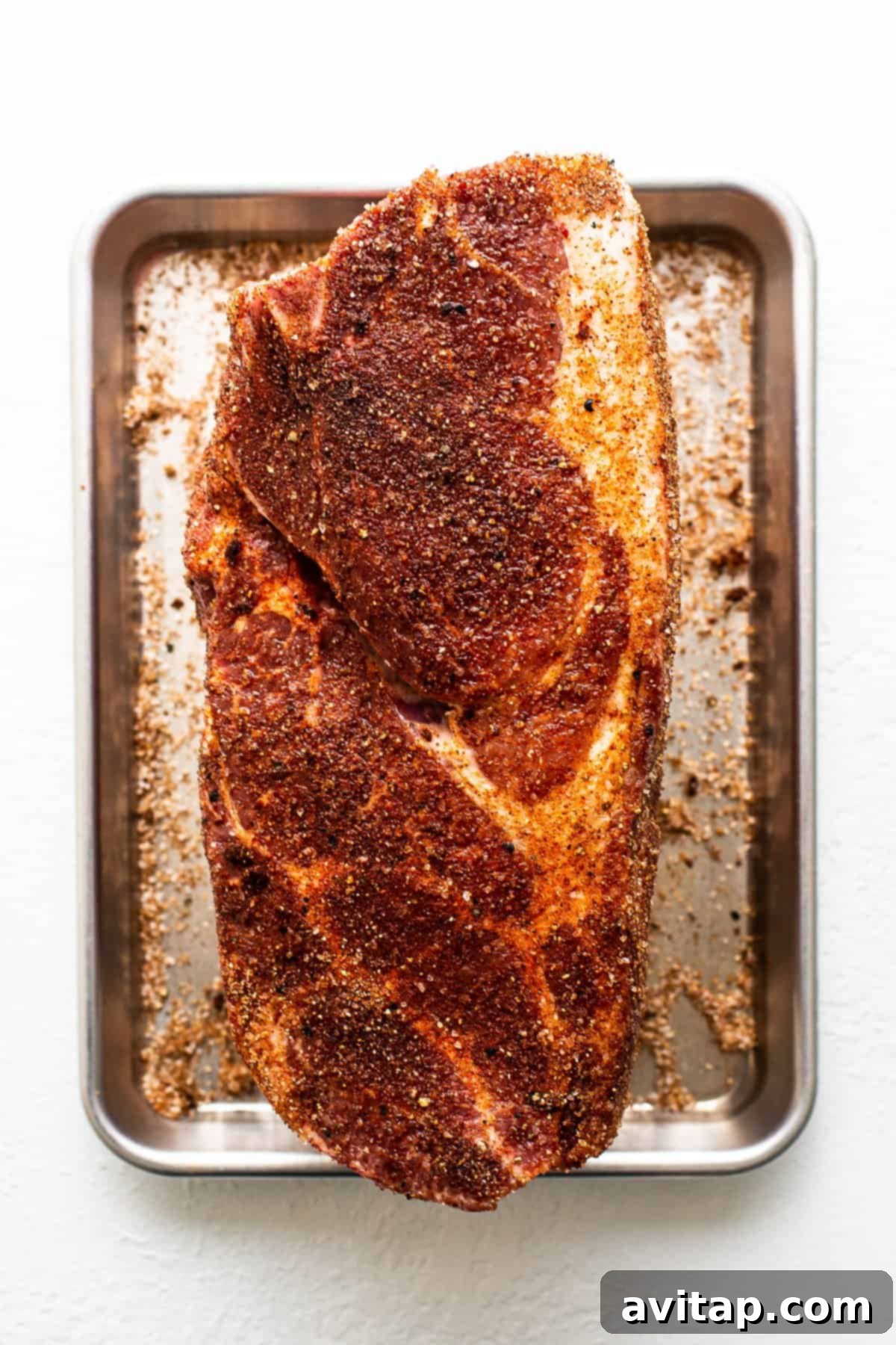 Tender Smoked Pork Shoulder 5 A generously seasoned pork shoulder, completely covered in a savory dry rub, placed on a tray, ready to absorb flavors before entering the smoker.