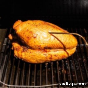 A turkey breast smoking on a smoker, surrounded by a gentle plume of smoke.
