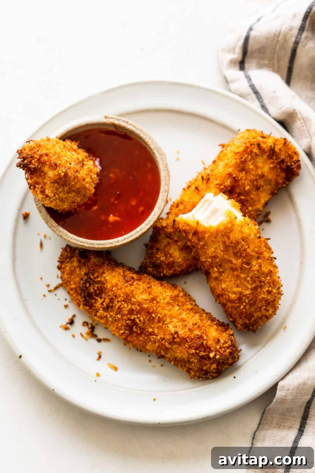 Crispy coconut chicken tenders on a plate with a dipping sauce, ready to be enjoyed.
