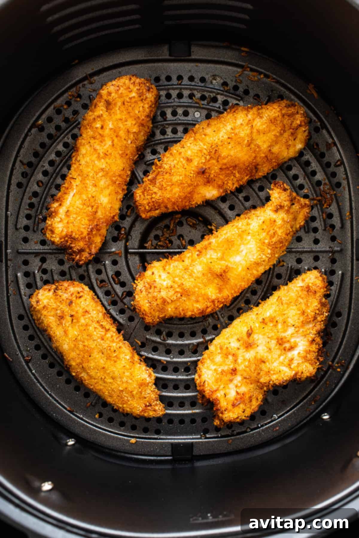 Cooked coconut chicken tenders cooling in an air fryer basket after achieving perfect crispiness.