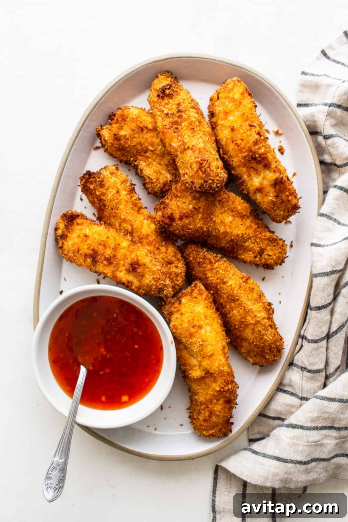 Air fryer coconut chicken tenders on a plate, served with a side of sweet chili sauce for dipping.