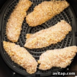Breaded chicken tenders neatly arranged in an air fryer basket, ready for cooking.