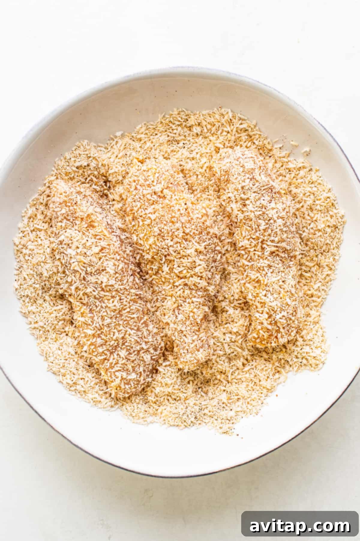 Raw chicken tenders breaded with a coconut and spice mixture, ready for air frying.