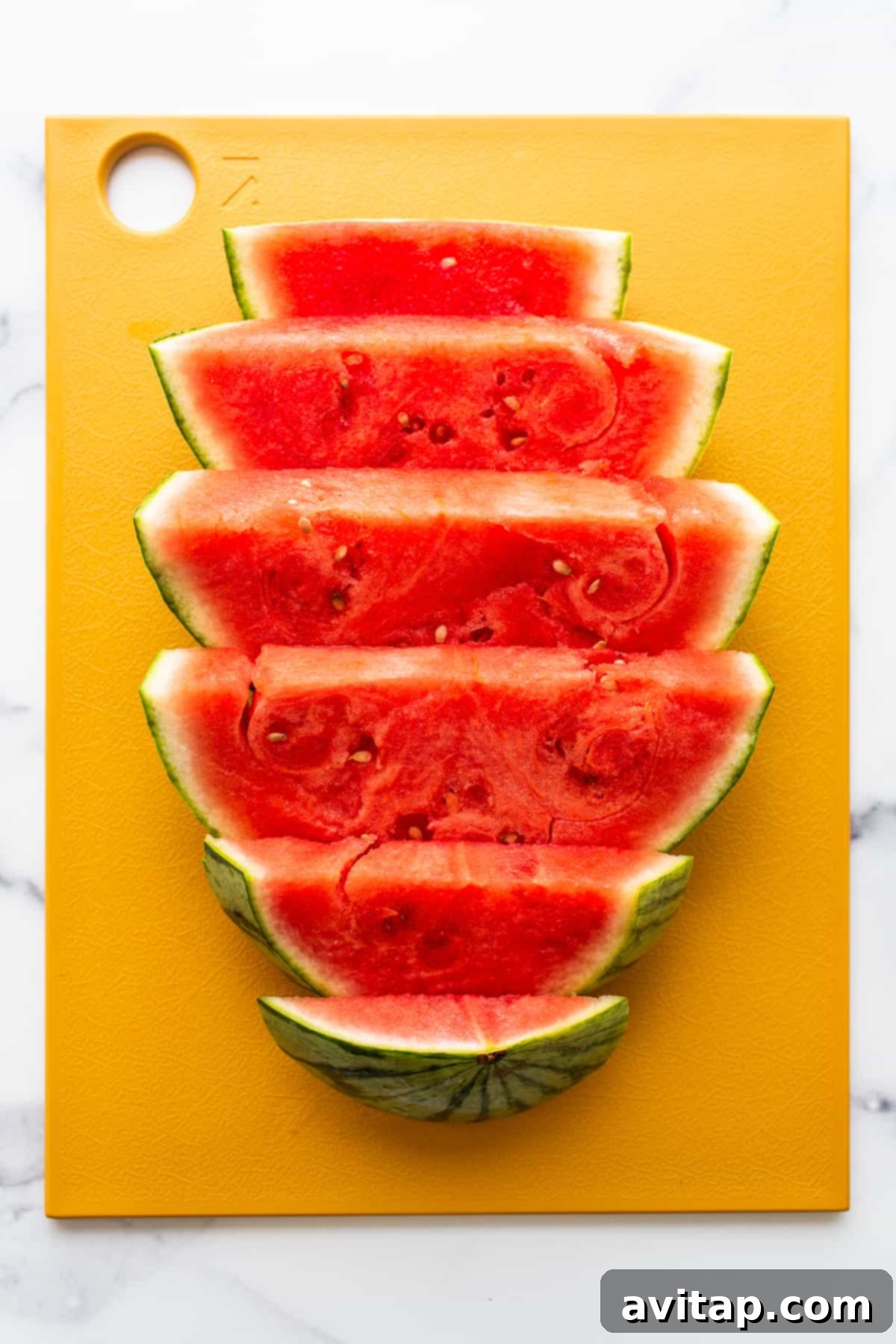 A freshly sliced watermelon on a wooden cutting board, ready for cubing into bite-sized pieces.