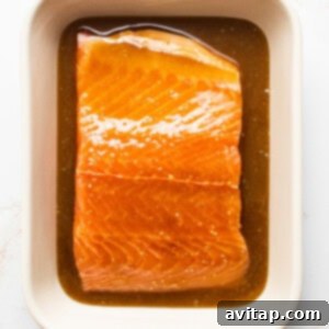 A pristine salmon filet marinating in the maple mustard sauce within a clear dish.