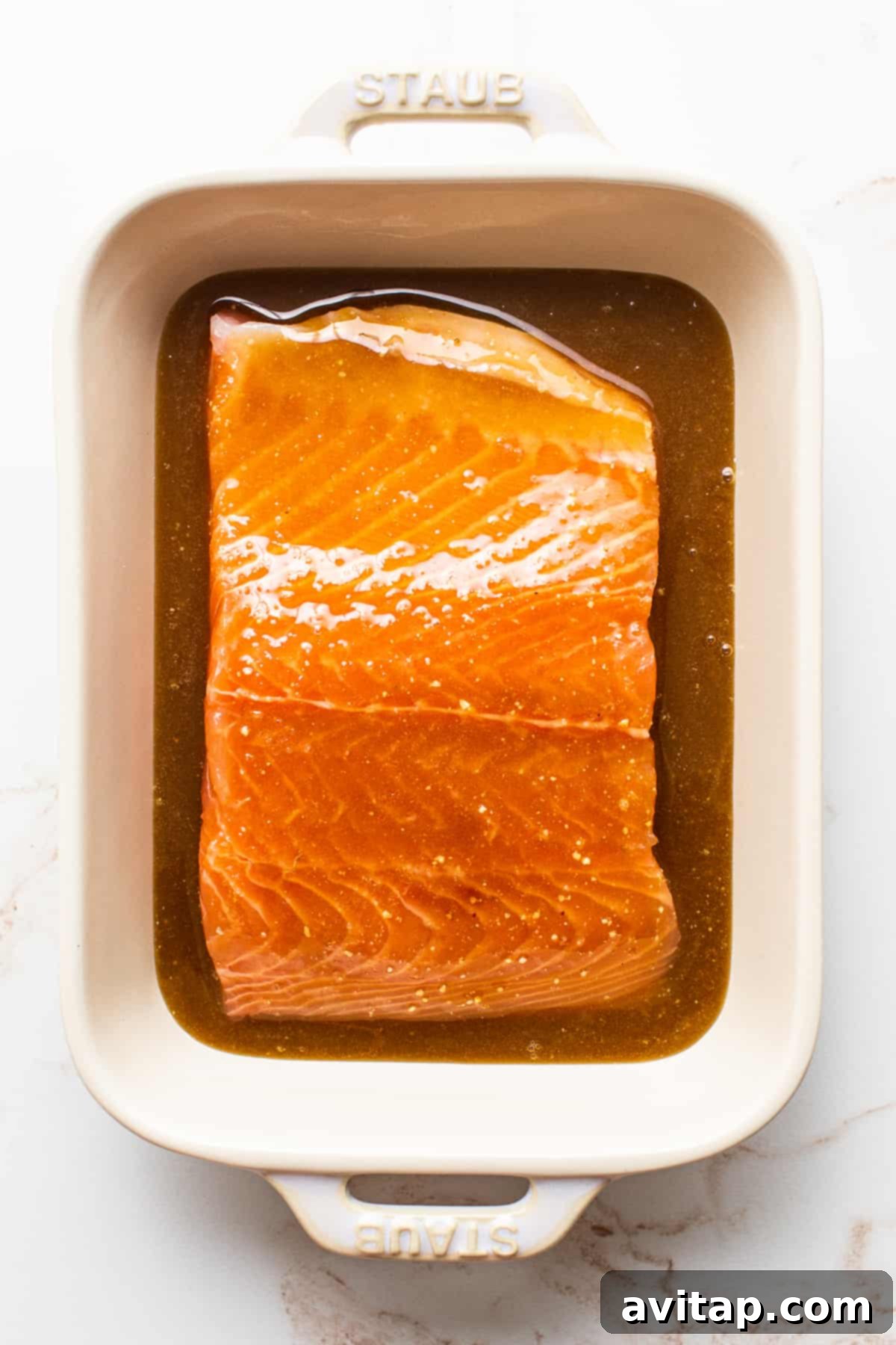 A pristine salmon filet soaking in a delightful maple mustard marinade within a clear dish, absorbing rich flavors.