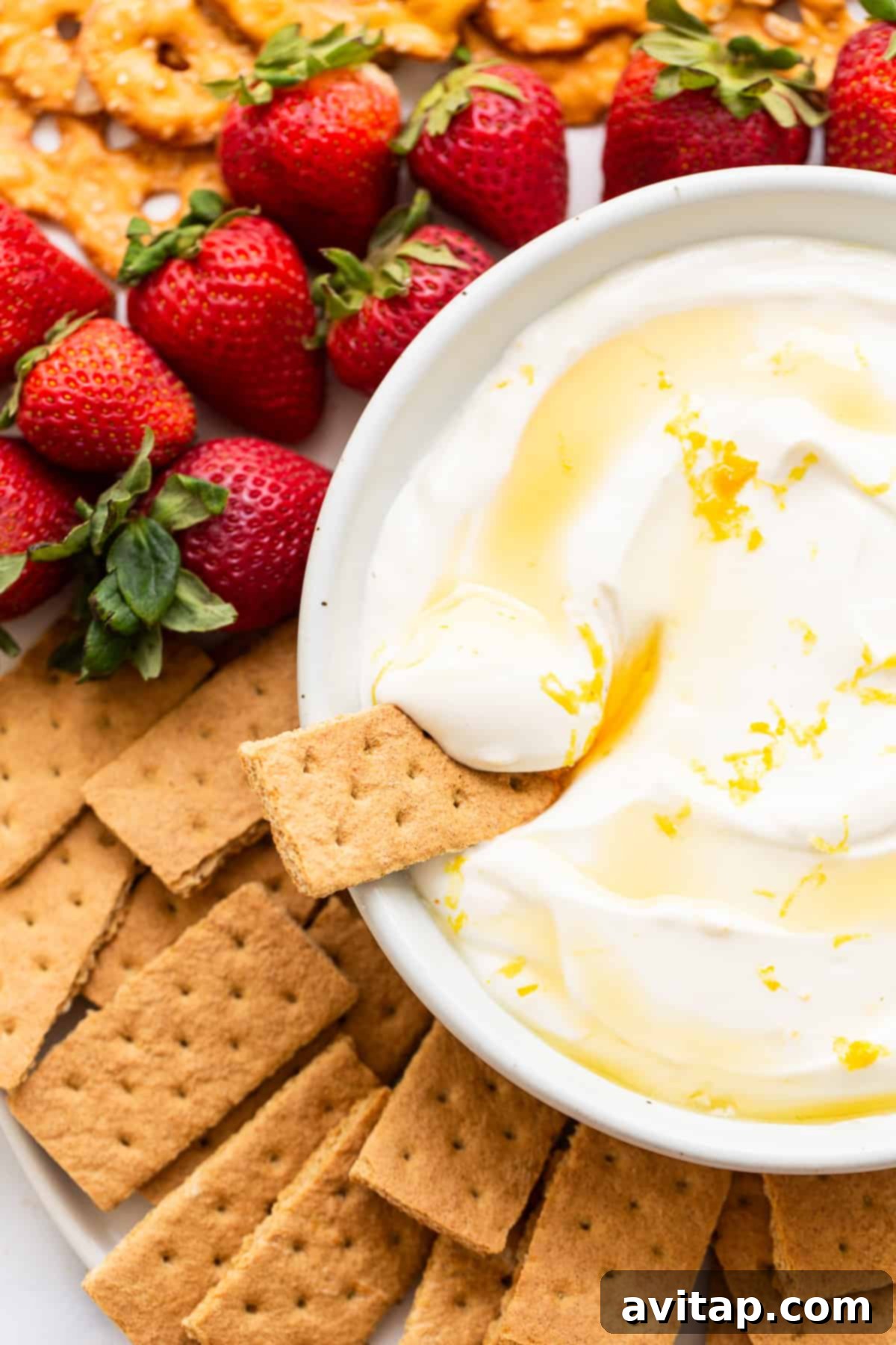 Creamy Greek yogurt fruit dip surrounded by fresh strawberries, blueberries, and graham crackers on a wooden board.