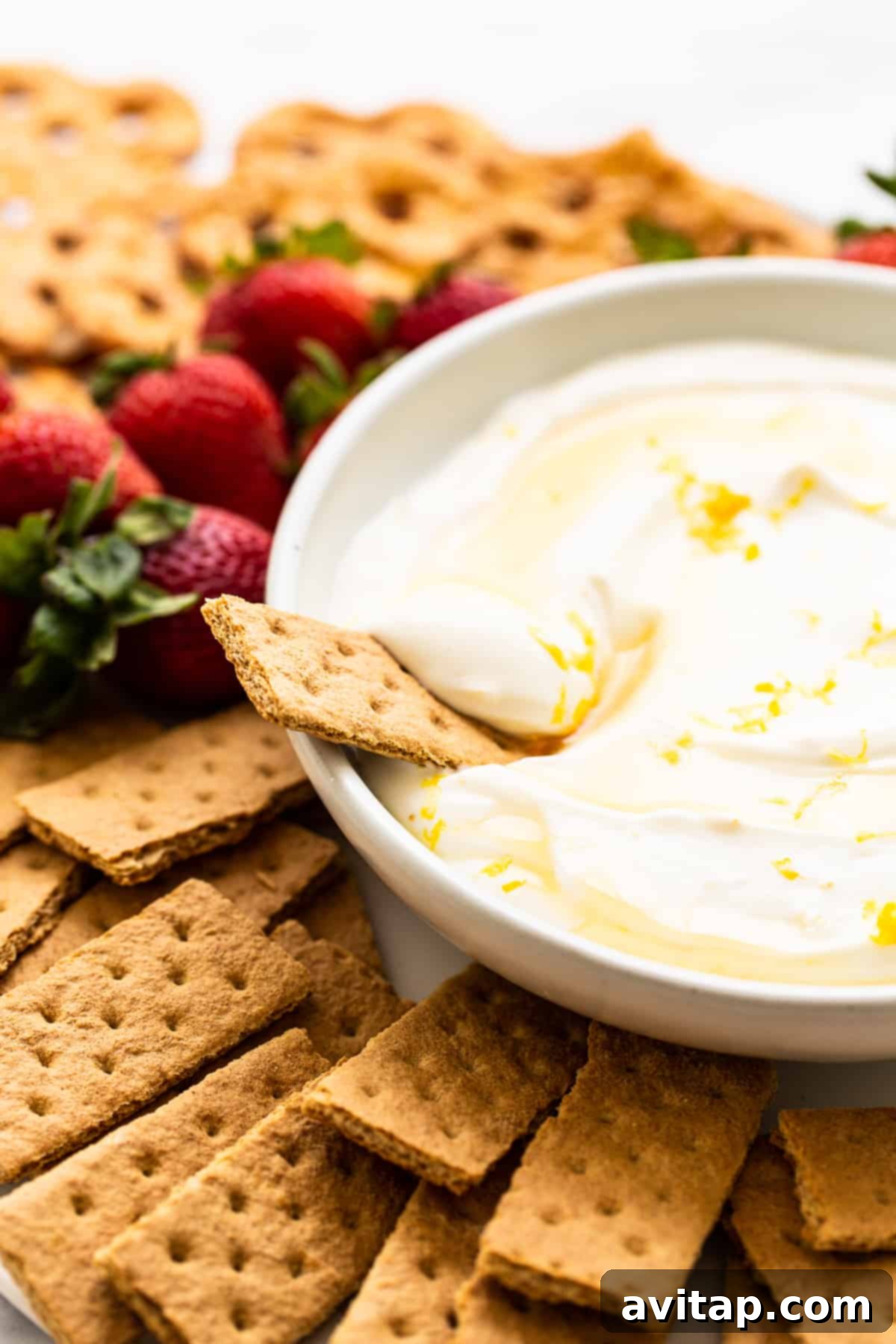 A close-up shot of creamy Greek yogurt fruit dip with a golden graham cracker perfectly dipped into its luscious texture, ready to be enjoyed.