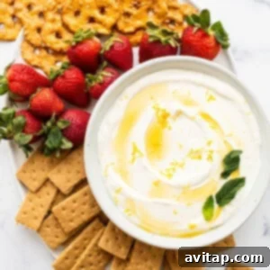 A beautifully presented bowl of creamy fruit dip surrounded by an assortment of fresh strawberries and crackers on a white plate, ready for serving.