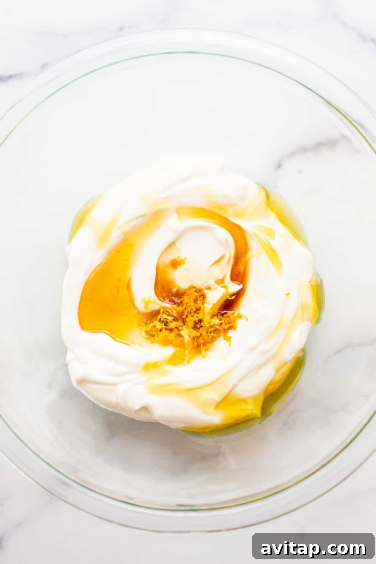 Close-up of creamy Greek yogurt with golden honey and vibrant lemon and orange zest in a white bowl, ready to be mixed for a delicious dip.