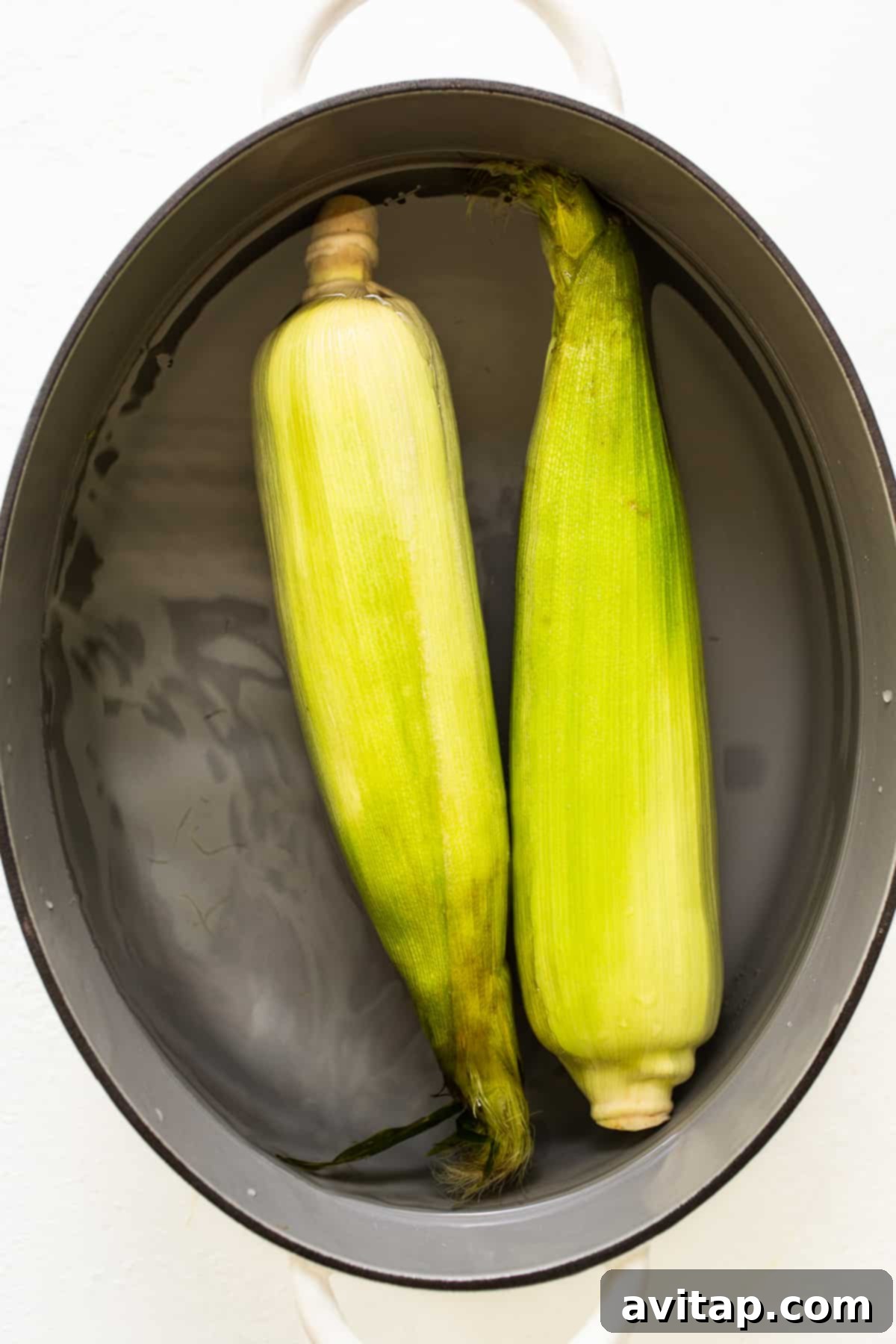 Prepping Corn: The Soaking Step for In-Husk Grilling Corn soaking in water, preparing for grilling in the husk.