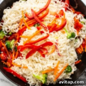 Ramen noodles being mixed with a medley of colorful vegetables in a large skillet.