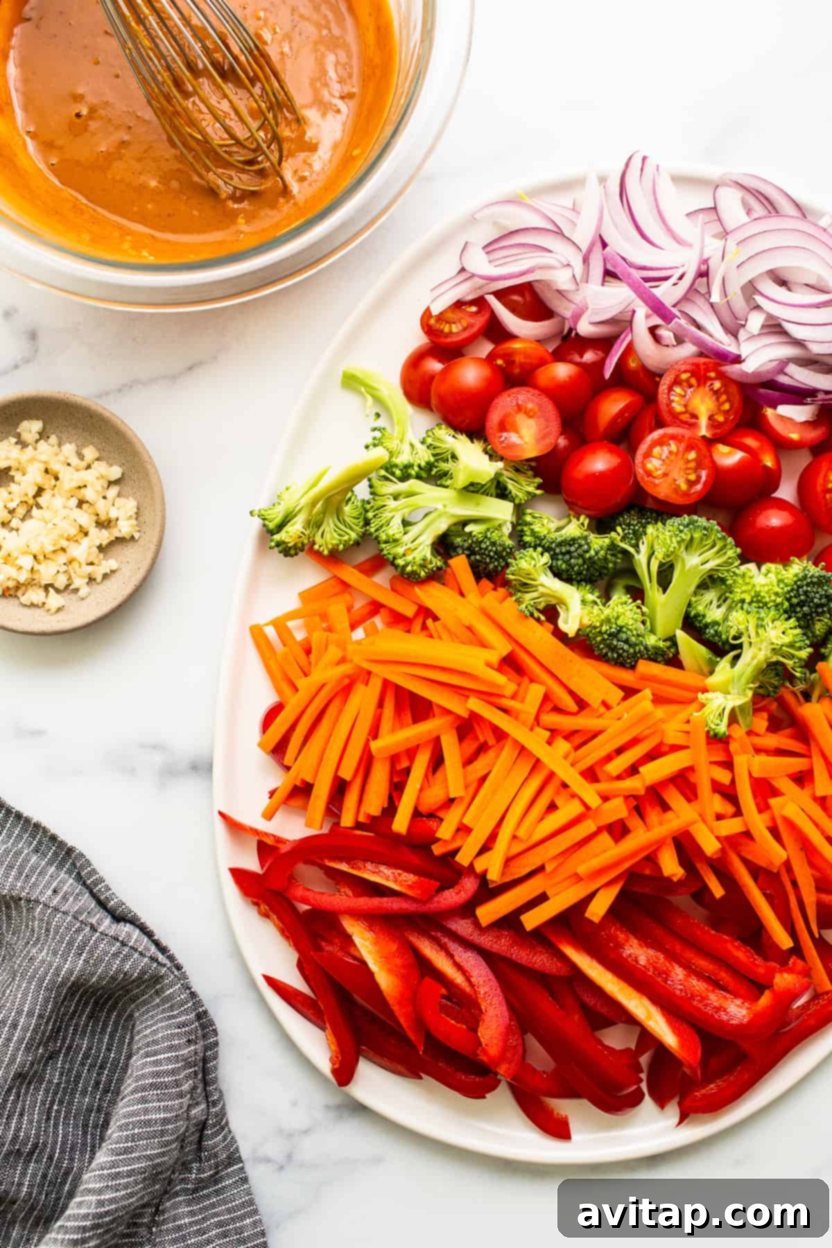 A vibrant platter of fresh, colorful vegetables including carrots, red bell peppers, broccoli florets, tomatoes, and onions, ready for the peanut noodles recipe.