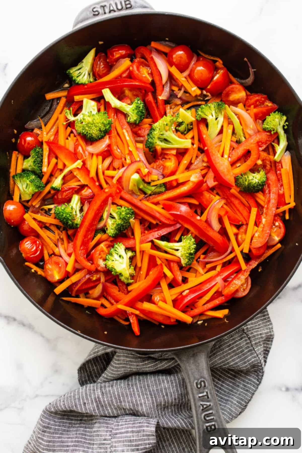 Assorted colorful vegetables being cooked in a large cast iron skillet, ready to be combined with noodles.