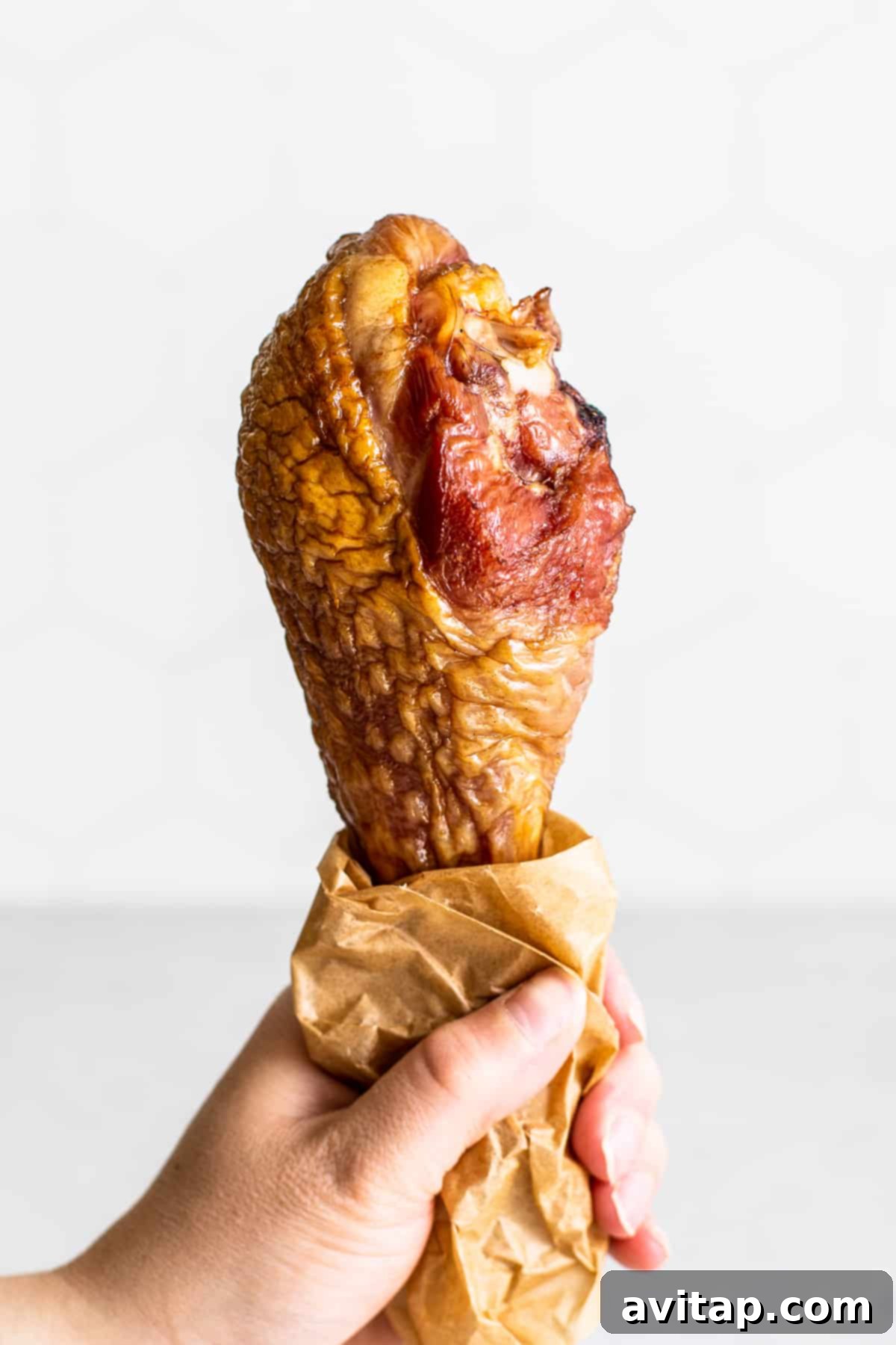 Tender Smoked Turkey Legs 2 A hand holding a perfectly smoked turkey leg, showcasing its golden-brown skin and juicy appearance.