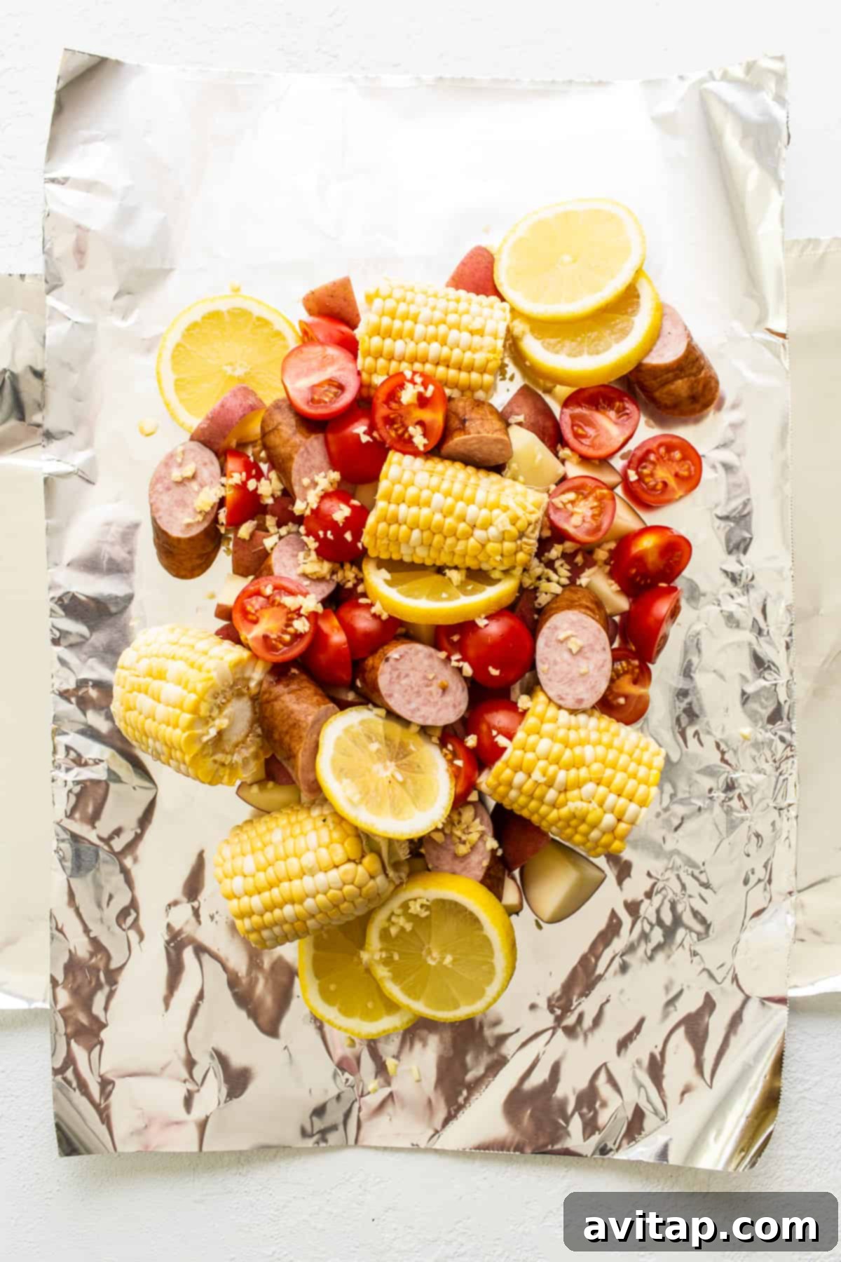 Easy Grilled Shrimp Parcels 3 Raw ingredients, including shrimp, potatoes, corn, and kielbasa, neatly arranged in an aluminum foil packet before grilling.