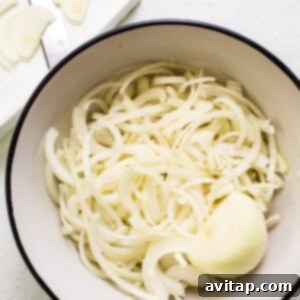 White onions in a bowl, uniformly sliced for optimal caramelization.