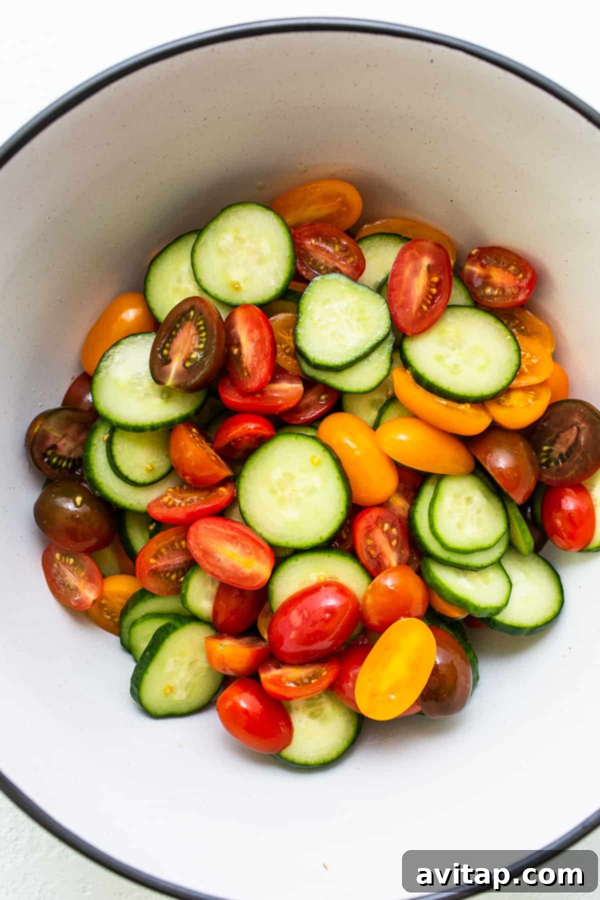 Tomatoes and cucumbers in a mixing bowl, ready to be salted.