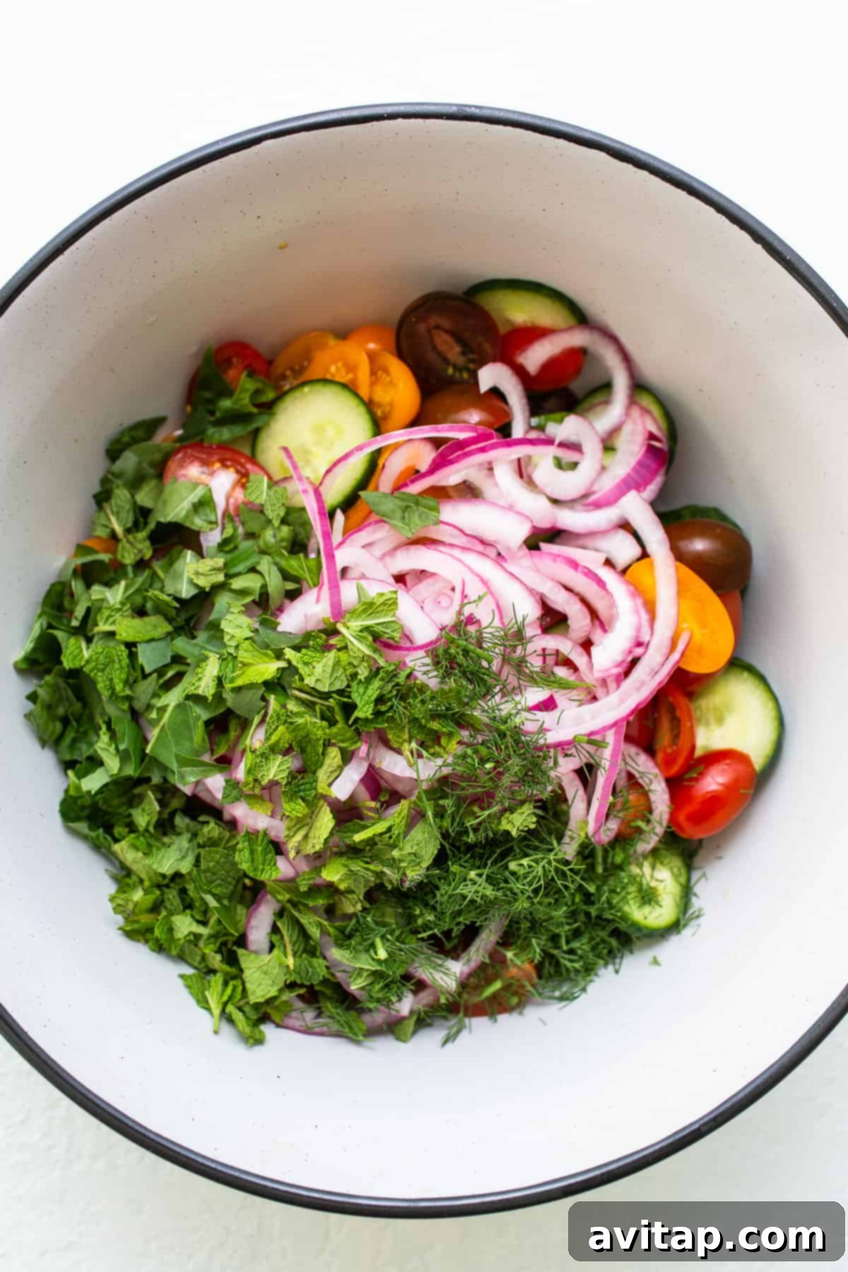 Cucumber salad in a bowl, tossed with fresh herbs and pickled onions.
