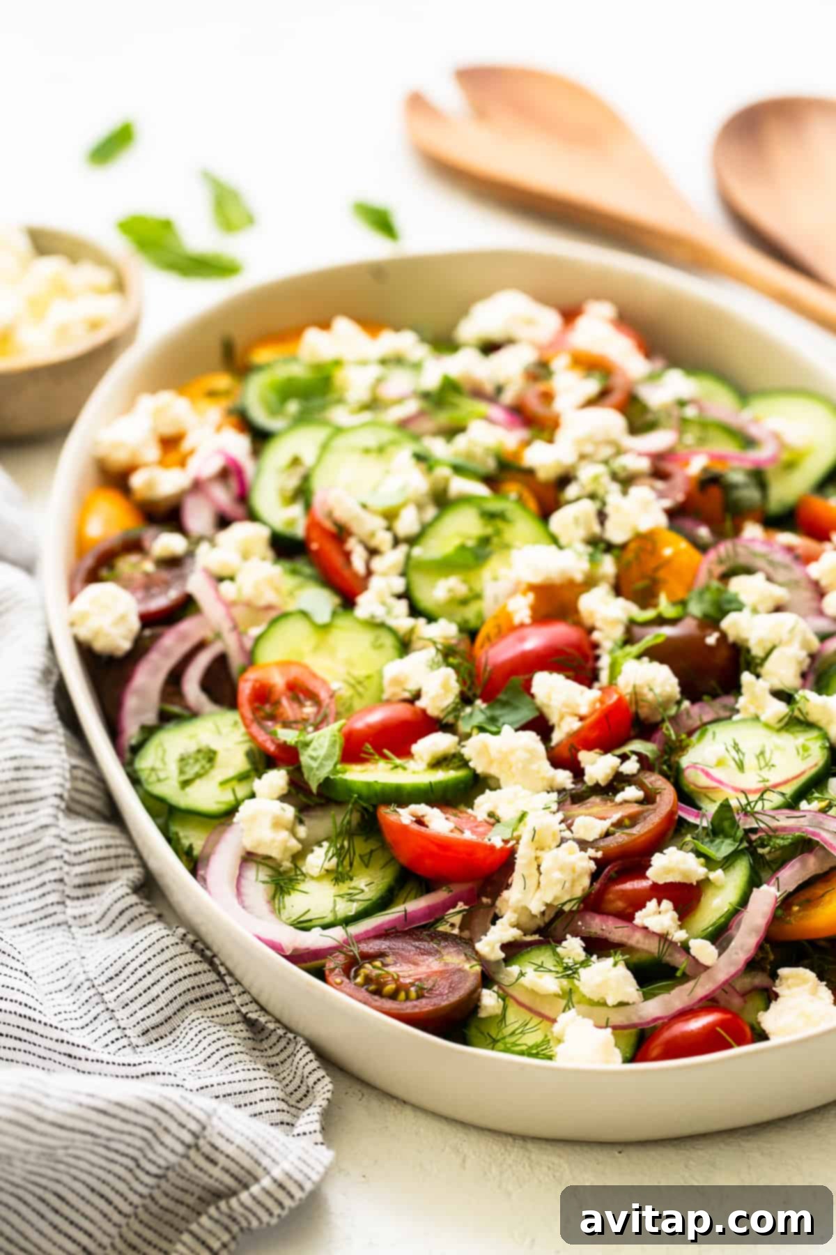 Vibrant Herb Cucumber Tomato Medley 6 A large serving bowl filled with herby cucumber tomato salad, generously topped with crumbled feta cheese and garnished with fresh herbs, ready to be served at a gathering.