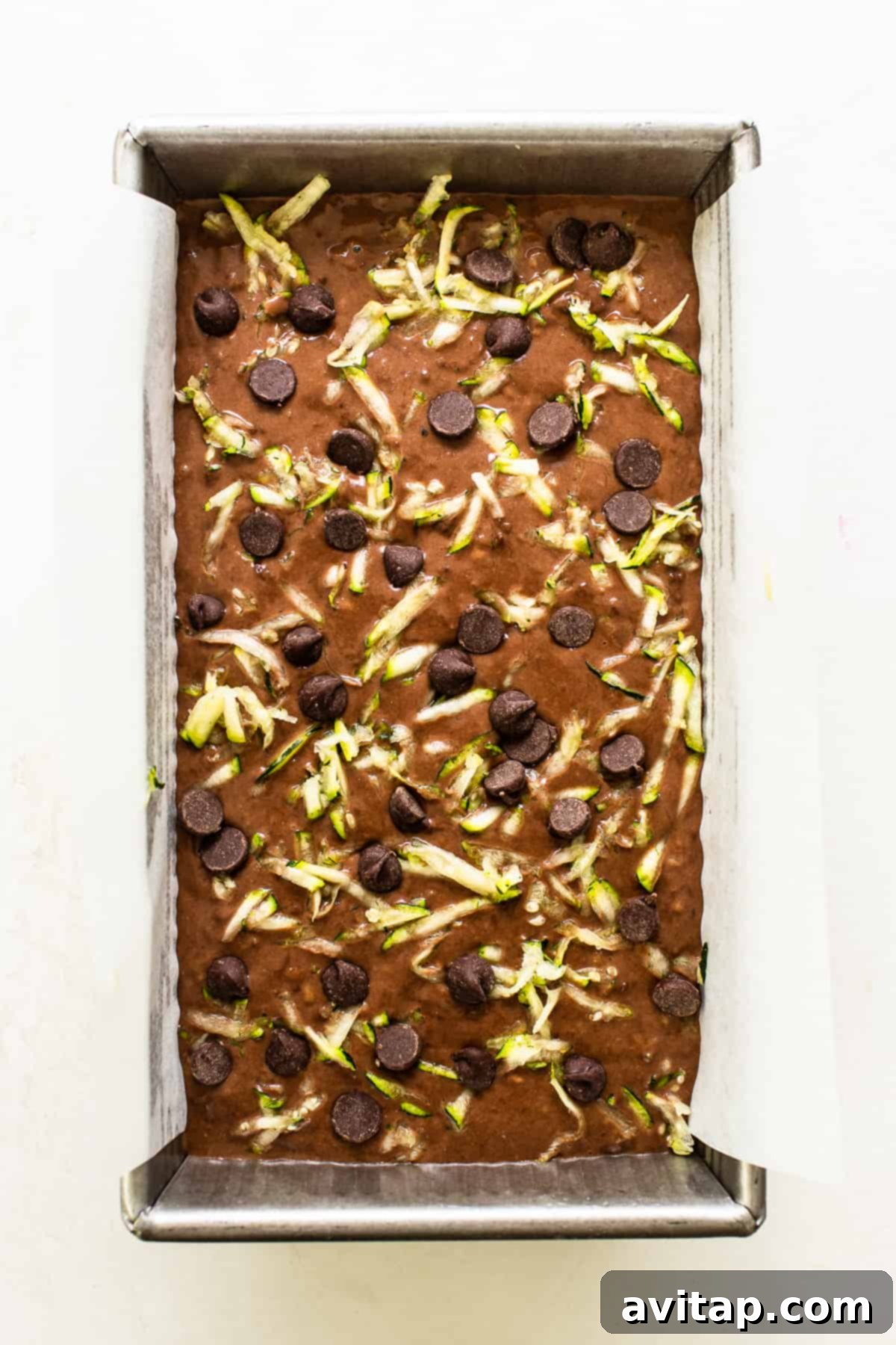 A loaf of chocolate zucchini bread, topped with chocolate chips, poised to go into the oven.