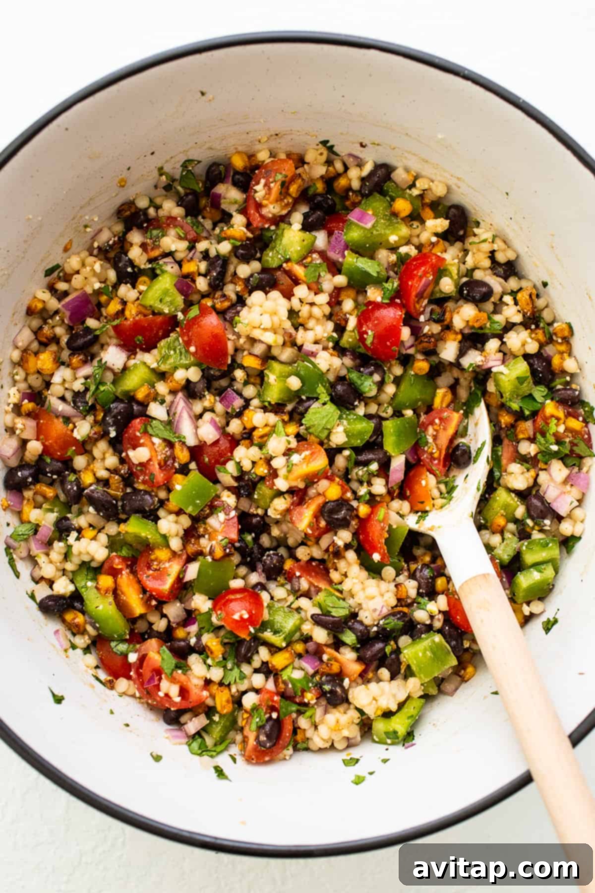 A delicious vegetarian Black Bean Couscous Salad recipe made with Israeli couscous, an abundance of fresh vegetables, black beans, and a zesty cilantro-lime vinaigrette. Vibrant Black Bean Couscous Salad in a bowl with a spoon, garnished with fresh cilantro and lime wedges.