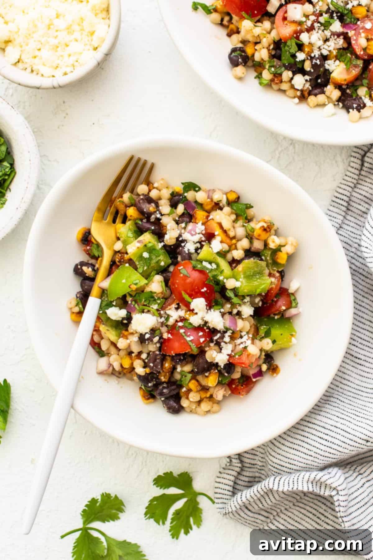 Enjoying a forkful of the delicious and healthy Black Bean Couscous Salad, a perfect vegetarian meal or side dish. A close-up of the Black Bean Couscous Salad in a white bowl with a fork, showing the vibrant ingredients and inviting textures.