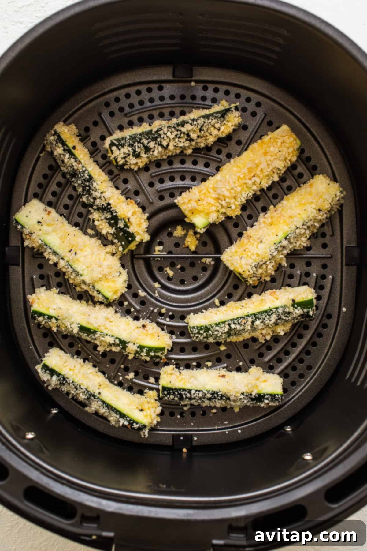 Air fryer basket filled with perfectly cooked, golden-brown zucchini fries.