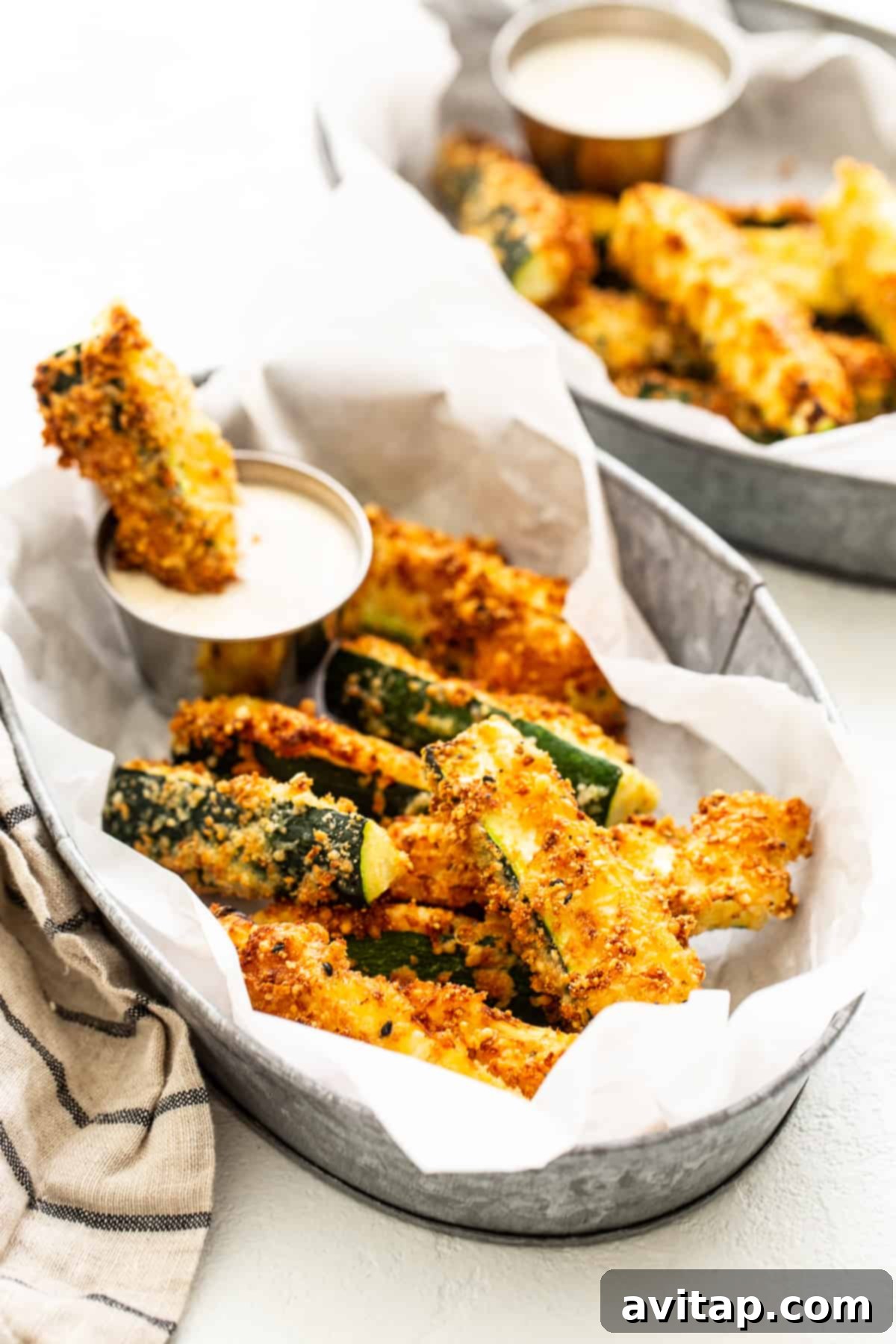 A basket overflowing with freshly cooked air fryer zucchini fries, garnished with fresh herbs.