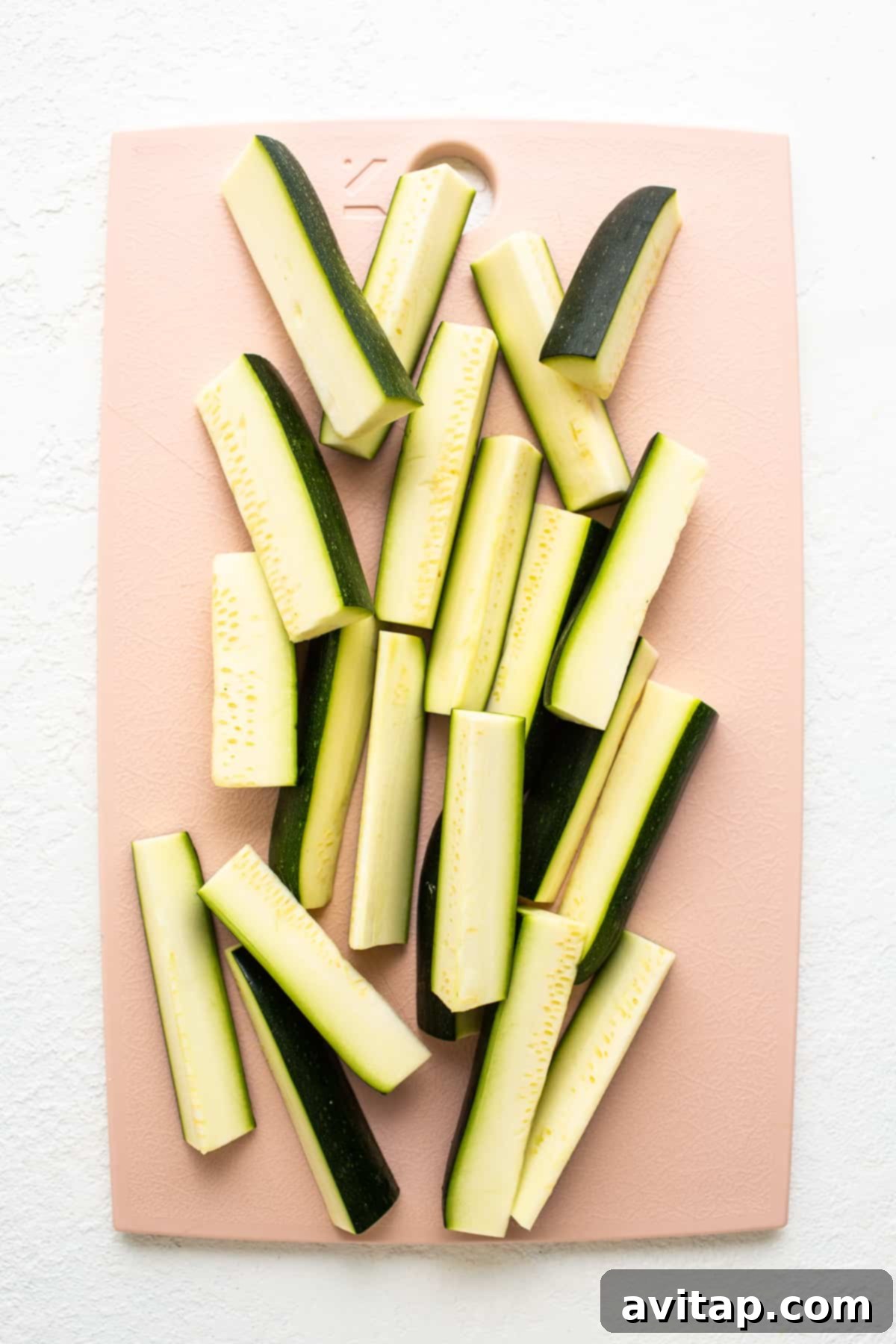 Fresh zucchini spears precisely cut on a wooden cutting board.