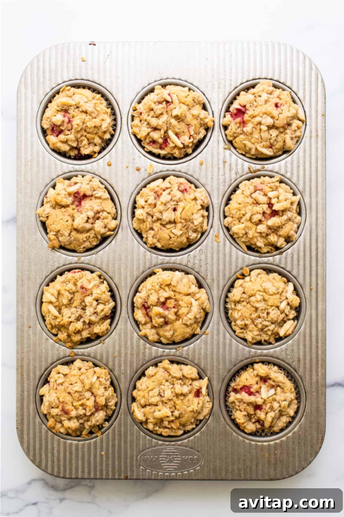 Freshly baked raspberry muffins cooling beautifully in a muffin tin, their golden streusel topping glistening, inviting a taste.