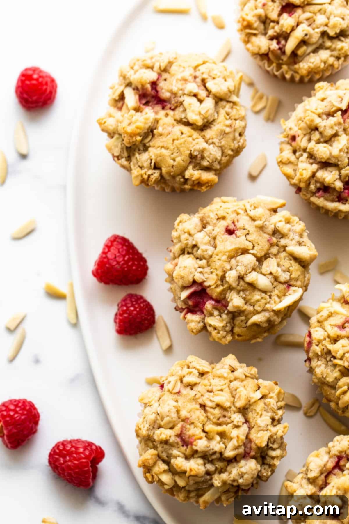 A freshly baked raspberry muffin, split in half, showcasing its fluffy interior and a generous amount of juicy raspberries, beautifully presented on a pristine white plate.