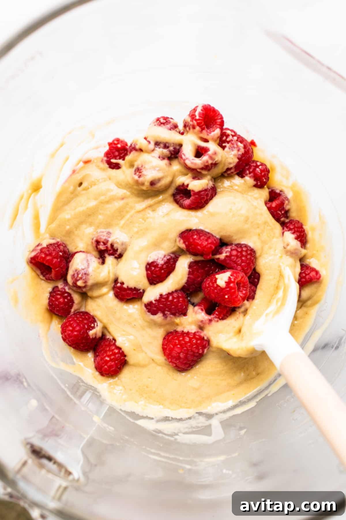 Smooth, vibrant raspberry muffin batter expertly mixed in a large glass bowl, showing the folded-in whole raspberries, ready to be scooped into muffin tins.