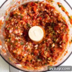 Salsa in a food processor after the second pulse, showing the spices and remaining tomato incorporated into the mix.