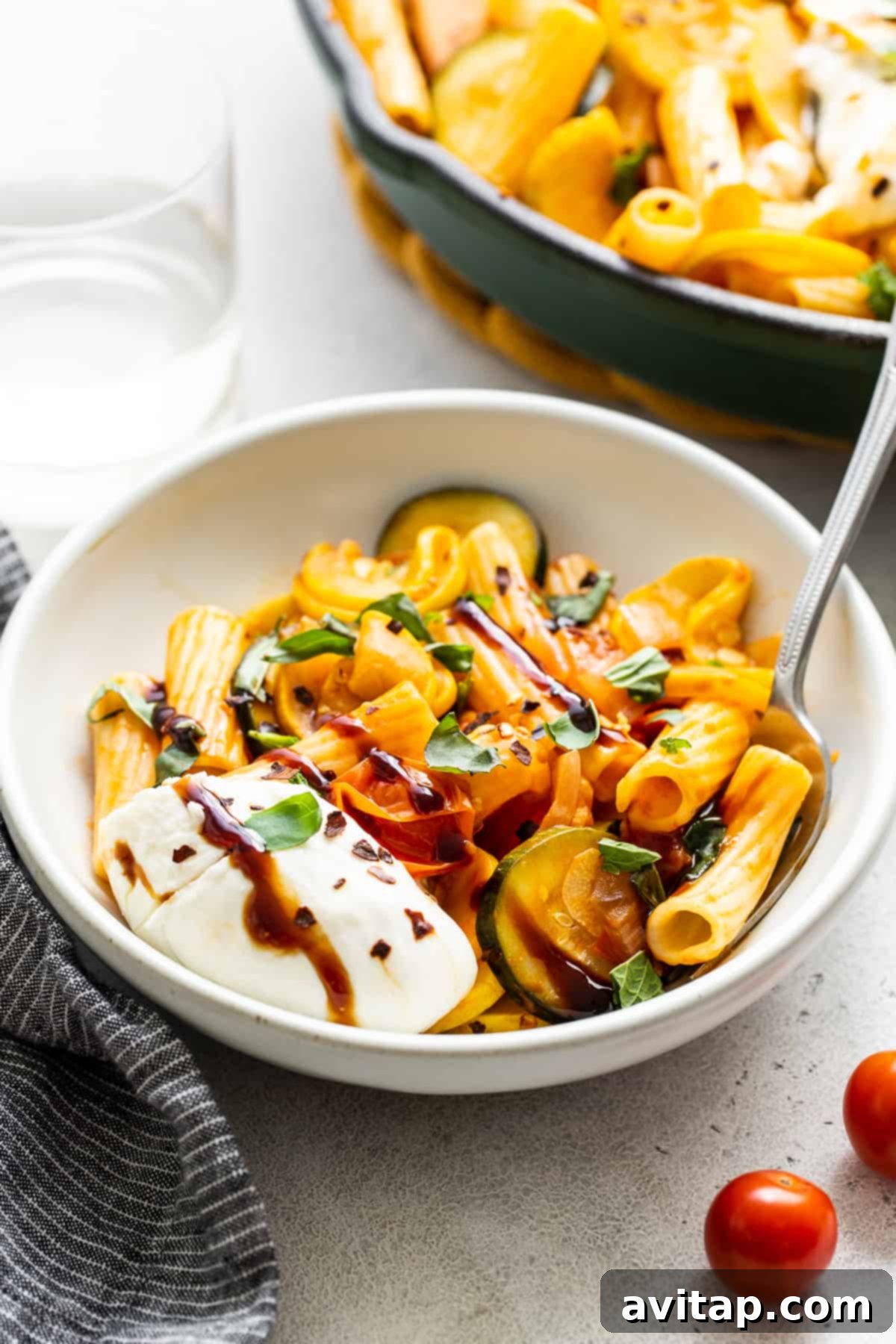 Summer squash pasta served in a bowl, generously topped with creamy burrata and fresh herbs.