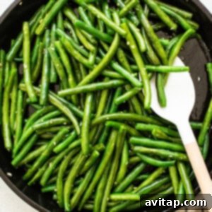 Vibrant green beans in a skillet with a wooden spoon, mid-sauté.