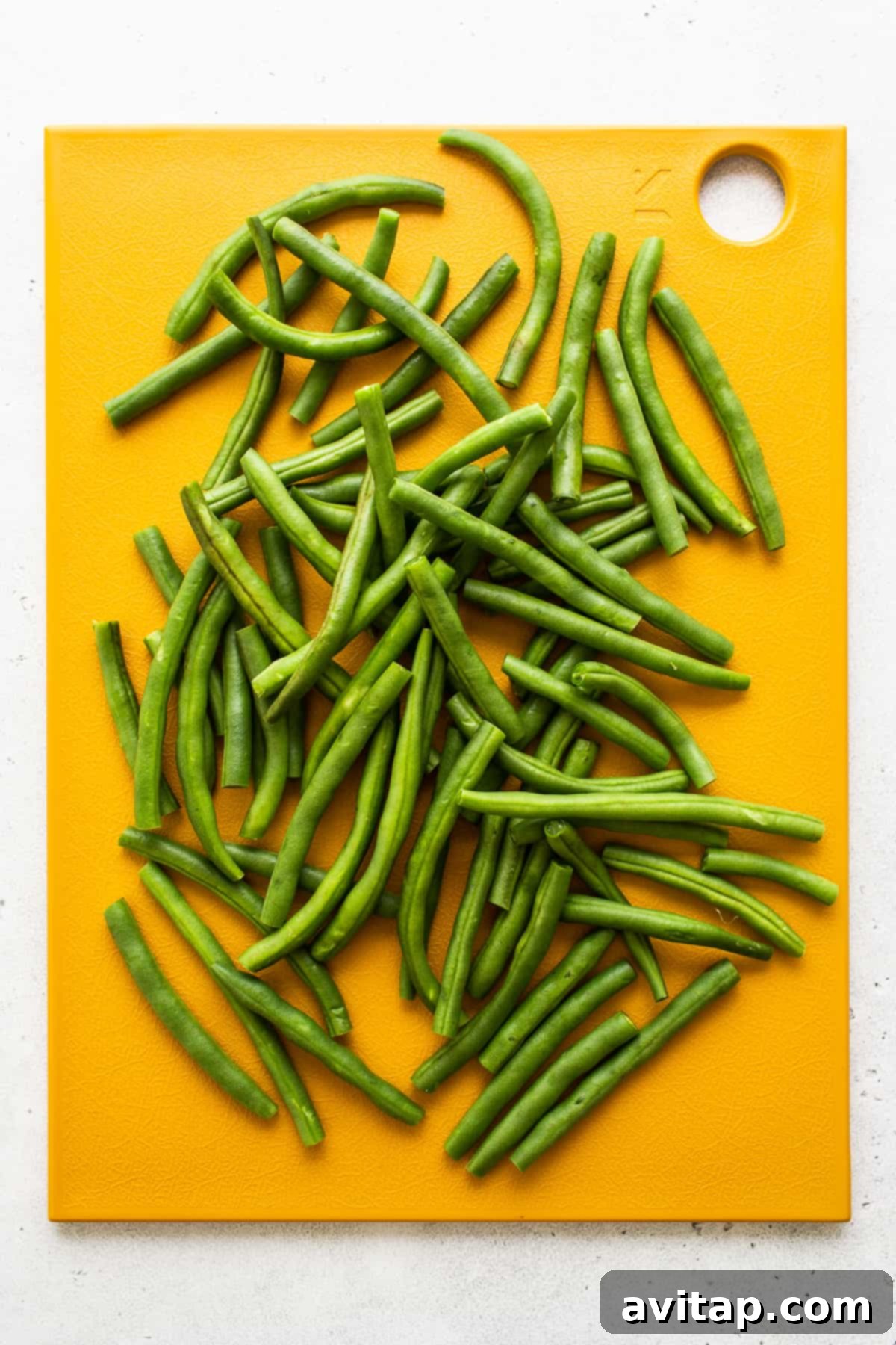 Freshly trimmed green beans neatly arranged on a wooden cutting board.
